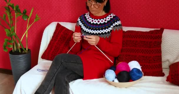 Femme mûre assise dans un canapé confortable et tricotant tout en appréciant le week-end à la maison, Femme âgée tricotant, se détendre à la maison faire une activité de passe-temps préférée le week-end, concept de bien-être - Séquence, vidéo