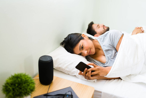 Unfaithful young woman in a relationship texting with her lover and cheating on her boyfriend. Girlfriend looking at her smartphone while her partner sleeps - Photo, Image