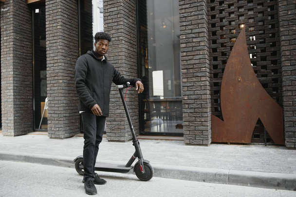 Active Leisure Concept. Side view of black male student driving stand-up scooter over brick road, copy space for ad or text - Foto, Bild