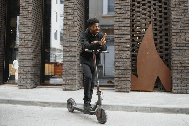 Active Leisure Concept. Side view of black male student driving stand-up scooter over brick road, copy space for ad or text - Foto, Bild