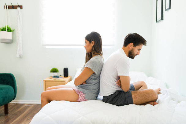 Angry couple in sleepwear ignoring each other in the bedroom. Upset girlfriend and boyfriend not talking because of a big fight - Photo, Image