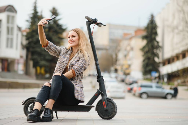 Beautiful young woman sitting on her electro scooter . - Foto, afbeelding