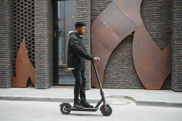 afro american guy rides an electric scooter against the background of a wall, a student uses eco transport - Foto, Bild