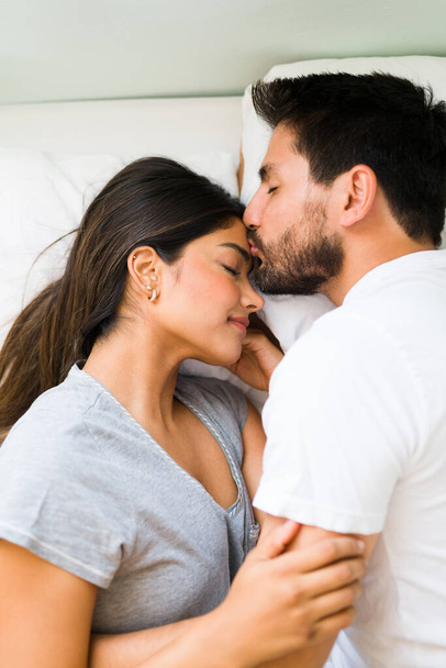 Tu és tudo para mim. Jovem apaixonado dando um beijo terno para sua namorada na testa enquanto deitado em uma cama confortável  - Foto, Imagem