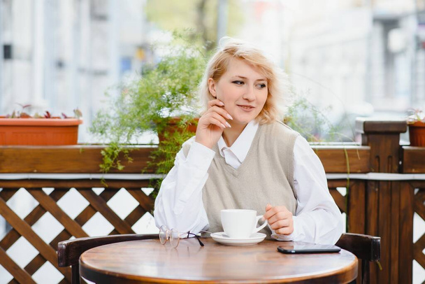 Fashion portrait of young woman siting at the table with cup of coffee, tea in street cafe. - Foto, Bild