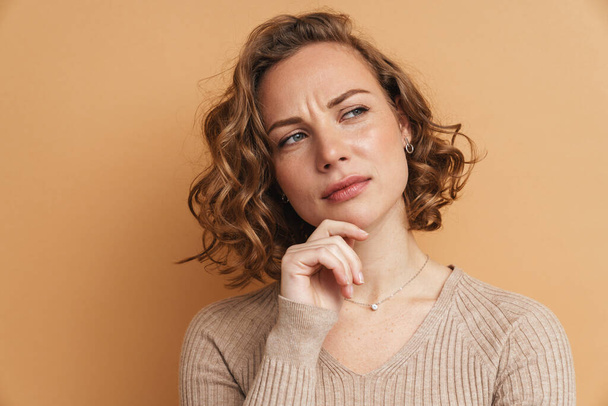 Young ginger puzzled woman frowning and looking aside isolated over beige background - Foto, immagini