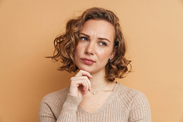 Young ginger puzzled woman frowning and looking aside isolated over beige background - Photo, Image