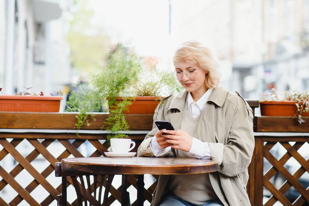 Retrato de moda de una joven sentada a la mesa con una taza de café, té en la cafetería de la calle. - Foto, Imagen
