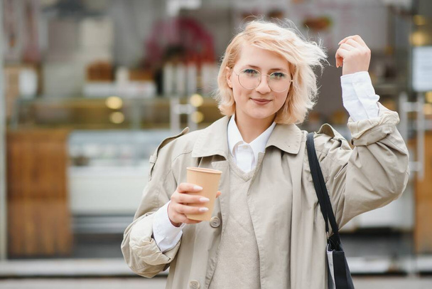 Cheerful stylish young woman in the street drinking morning coffee in sunshine light. - Foto, Imagen