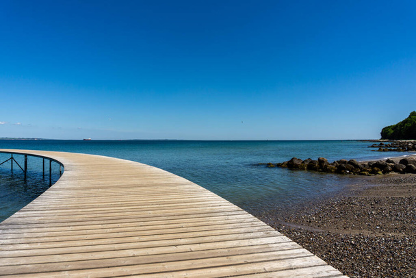 Un paseo marítimo curvado de madera conduce al océano azul - Foto, Imagen