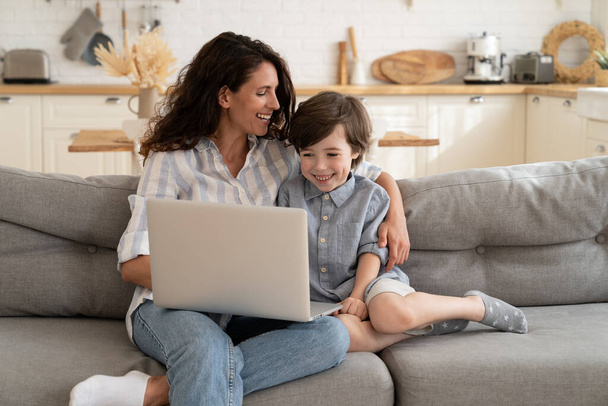 Young single mother relax after work with cute preschool son watching funny video or movie on laptop - Photo, Image