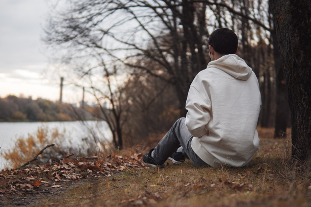 Un giovane solitario siede sulla riva del fiume tardo autunno cupo e nuvoloso - Foto, immagini