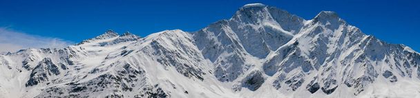 チェゴからのコーカサス山脈のパノラマビュー、高さ3050メートル、カバルディノ・バルカリア、ロシア。青空に向かって雪をかぶった山の写真. - 写真・画像