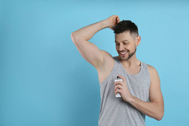 Handsome man applying deodorant on turquoise background. Space for text - Fotó, kép