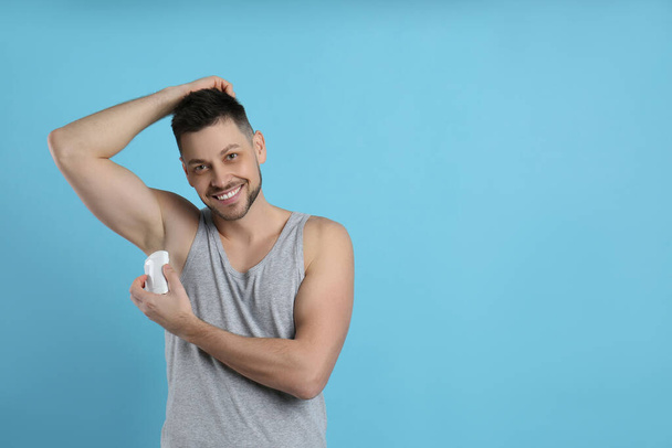 Handsome man applying deodorant on turquoise background. Space for text - Fotó, kép
