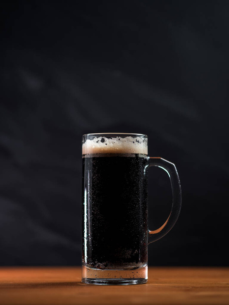 Bier mok van verse stout op een houten tafel, donkere achtergrond - Foto, afbeelding