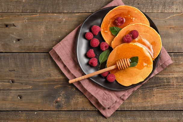 Gearomatiseerde pannenkoeken met honing en verse frambozen als ontbijt. Geweldig ontbijt dessert, versierd met verse munt bladeren. - Foto, afbeelding