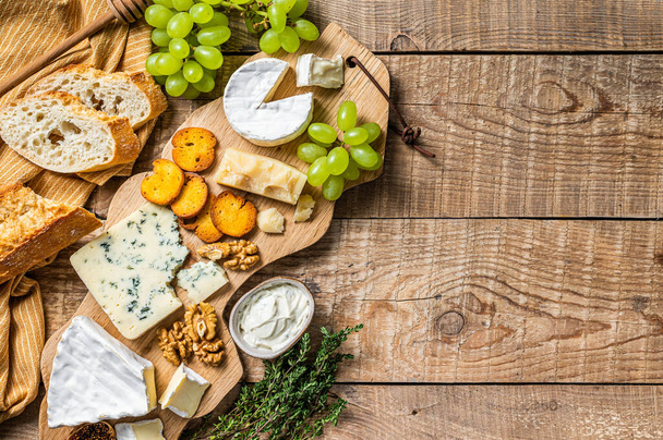 Cheese Board. Brie, Camembert, Roquefort, parmesan et fromage à la crème bleu avec raisin, figue, pain et noix sur planche de bois. fond en bois. Vue de dessus. Espace de copie - Photo, image