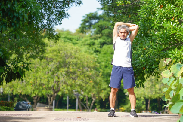 älterer Herr lächelnd, Läufer beim Aufwärmen, indem er bei guter Stimmung in der Morgensonne die Arme im Park ausstreckt, Konzept alternde Gesellschaft, gute Gesundheit, Lebensqualität.                                - Foto, Bild