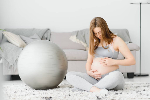 Young pregnant woman exercising yoga with fit ball at home - Fotografie, Obrázek