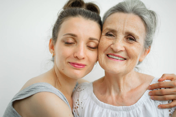 Glückliche Seniorin umarmt ihre erwachsene Tochter, die Frauen lachen zusammen, aufrichtige Familie unterschiedlichen Alters hat Spaß auf weißem Hintergrund - Foto, Bild