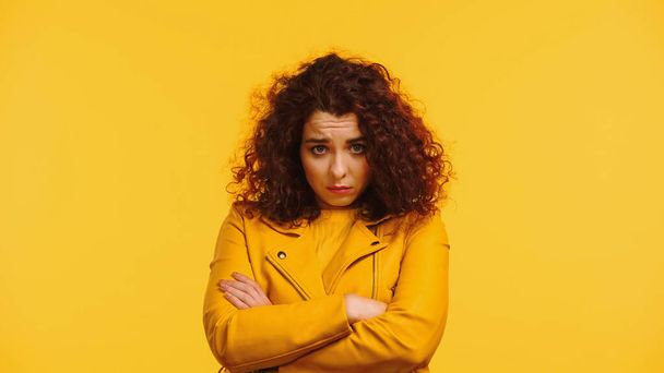 offended young woman in leather jacket standing with crossed arms isolated on yellow - Фото, изображение