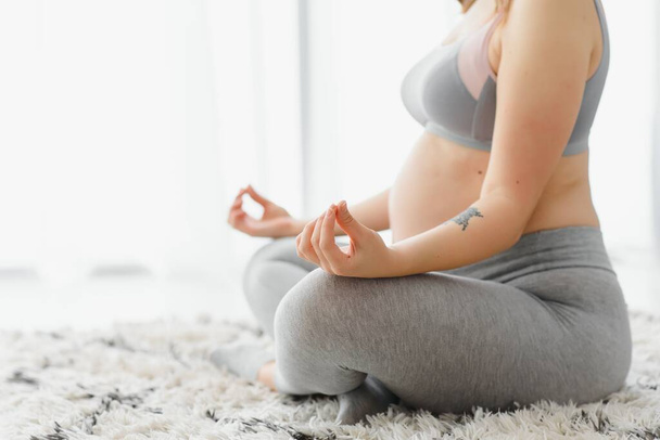 Closeup shot of unrecognizable pregnant woman meditating at home, expetcant lady sitting in lotus position with clasped hands, practicing yoga for healthy pregnancy, cropped image with free space - Фото, изображение