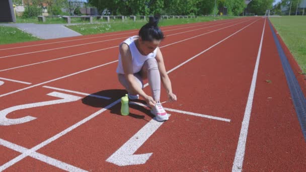 Mujer está atando sus zapatos en una pista de atletismo del estadio - Metraje, vídeo