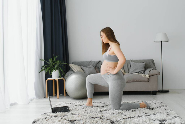 Healthy Pregnancy Yoga and Fitness concept. Young pregnant yoga woman working out in living room interior. - Foto, Imagen
