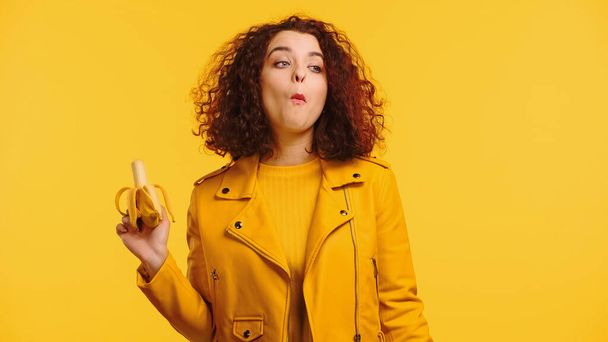 jonge vrouw in jas eten banaan geïsoleerd op geel  - Foto, afbeelding
