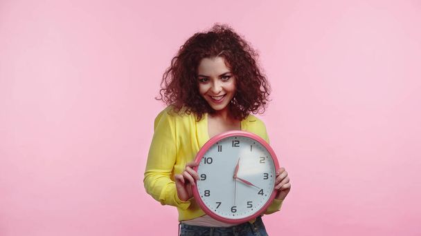 glückliche junge Frau hält Uhr isoliert auf rosa  - Foto, Bild
