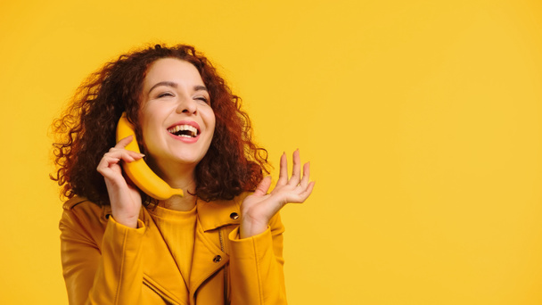 göndör nő utánozza telefonbeszélgetés banán és mosolygós elszigetelt sárga - Fotó, kép