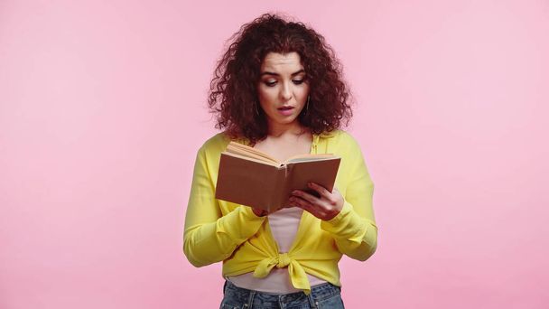 curly and surprised student reading book isolated on pink  - Foto, Bild