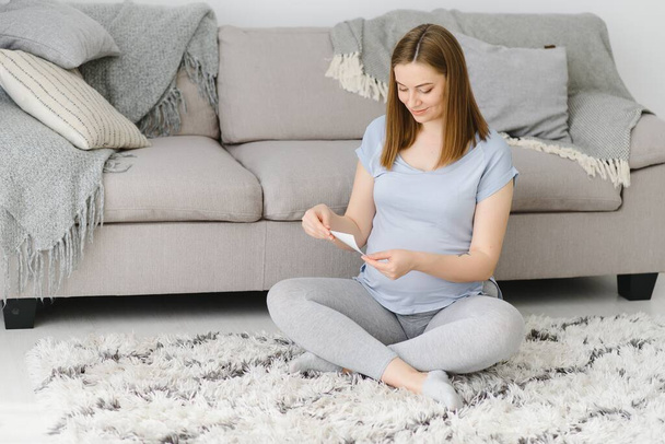 Pregnant woman looking at her baby sonography. Happy expectant lady enjoying first photo of her unborn child, anticipating her future life, copy space - Фото, изображение