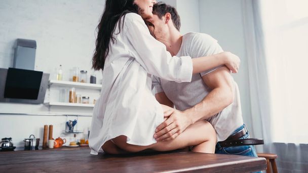 young man embracing woman in white shirt on kitchen table - Foto, Imagem