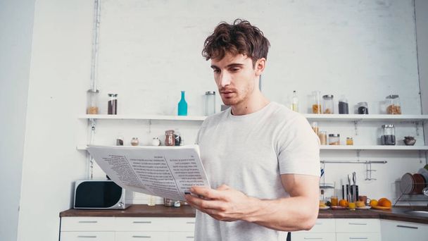 young man in white t-shirt reading newspaper in kitchen - 写真・画像
