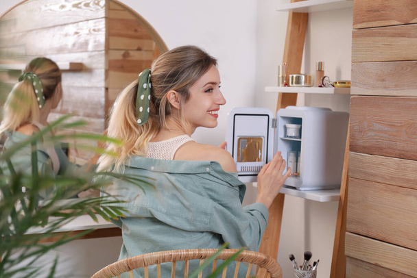 Женщина берет косметический продукт из мини-холодильника в помещении - Фото, изображение