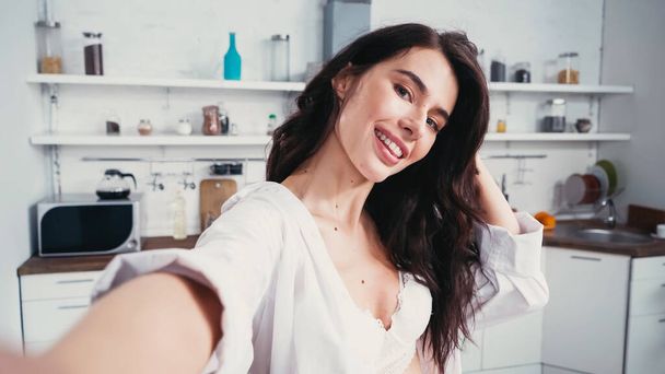 Seksikäs nainen valkoisessa paidassa hymyilee ottaessaan selfie hämärtynyt etualalla - Valokuva, kuva