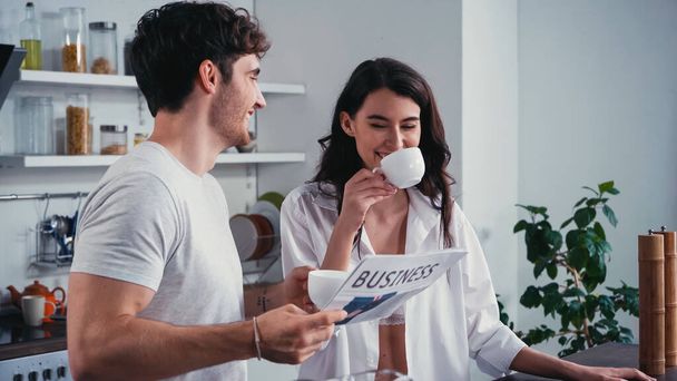 smiling man holding business newspaper near happy woman drinking morning coffee - Photo, Image