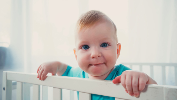 baby boy with blue eyes looking at camera from white crib  - Photo, Image