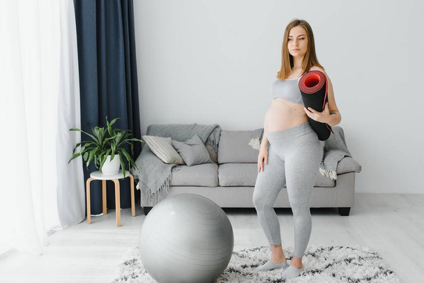 Healthy Pregnancy Yoga and Fitness concept. Young pregnant yoga woman working out in living room interior. - Foto, Bild