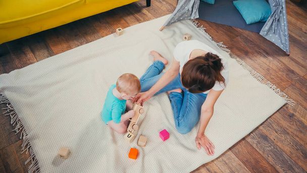 vista superior de la madre descalza sentada cerca del niño jugando con juguetes  - Foto, Imagen