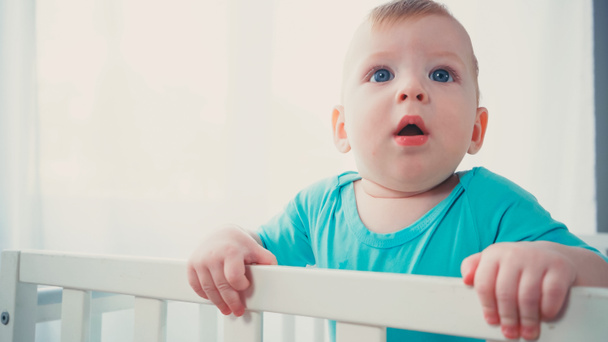 sorprendido bebé niño de pie en la cuna del bebé y mirando hacia arriba - Foto, Imagen