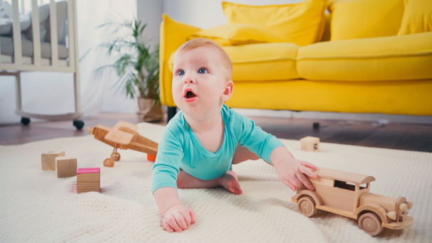 Junge mit blauen Augen sitzt auf Decke und spielt mit Holzspielzeugauto - Foto, Bild
