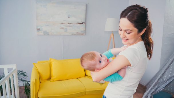 cheerful mother nursing baby boy in living room - Photo, Image