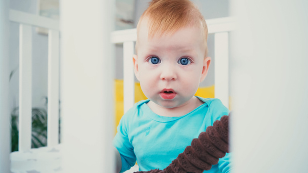 infant boy sitting in blurred baby crib with soft toy - Fotografie, Obrázek