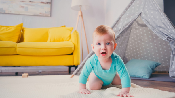 glücklicher kleiner Junge krabbelt auf Decke in der Nähe von Tipi im Wohnzimmer  - Foto, Bild