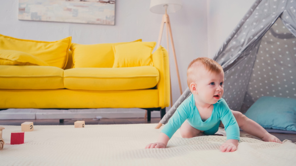 Младенец в синем комбинезоне ползает по одеялу возле Типи в гостиной  - Фото, изображение