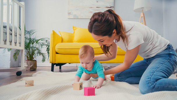 happy mother looking at infant son playing with cubes on blanket  - Foto, Imagem