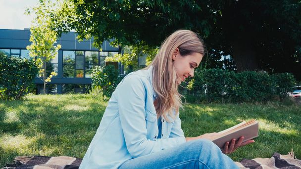 Parkta kitap okuyan neşeli genç bir kadının yan görünüşü - Fotoğraf, Görsel